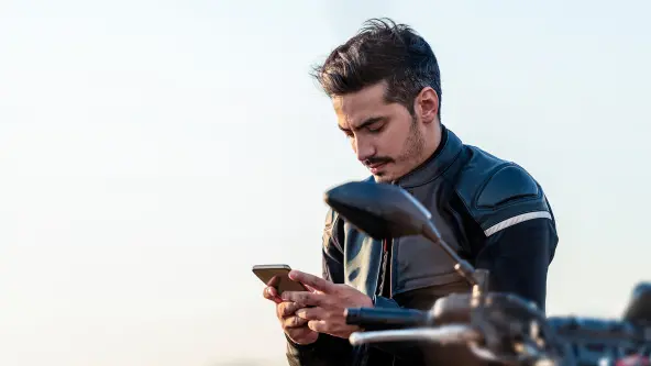 Mann mit Motorradoutfit blickt auf Handy in der Hand